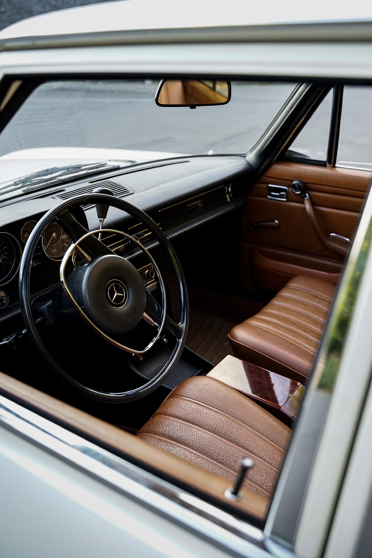 Blick durch das offene Fenster eines Oldtimers auf Lenkrad, braune Ledersitze und Holzverkleidung